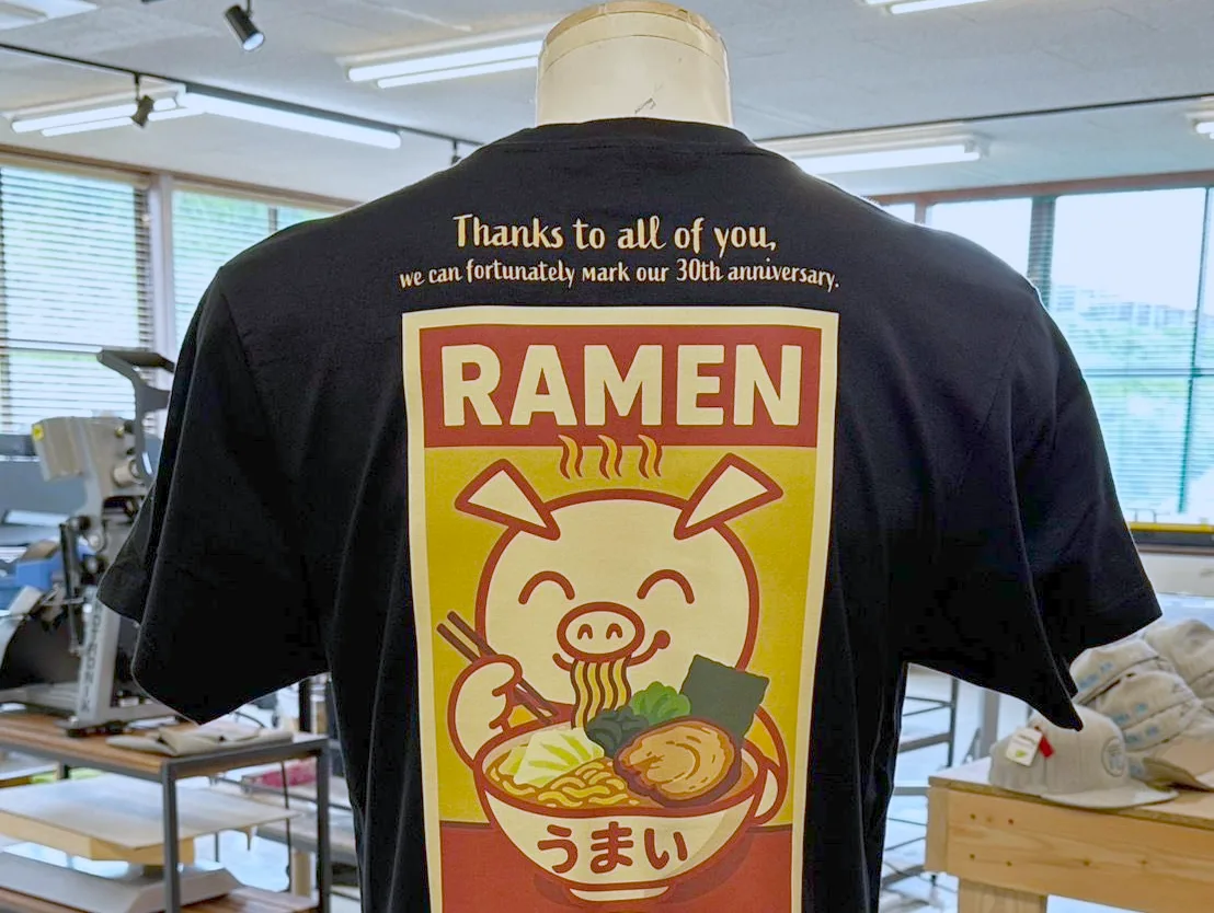 おそろいのフルカラープリントのTシャツを着た30人ほどのグループ
