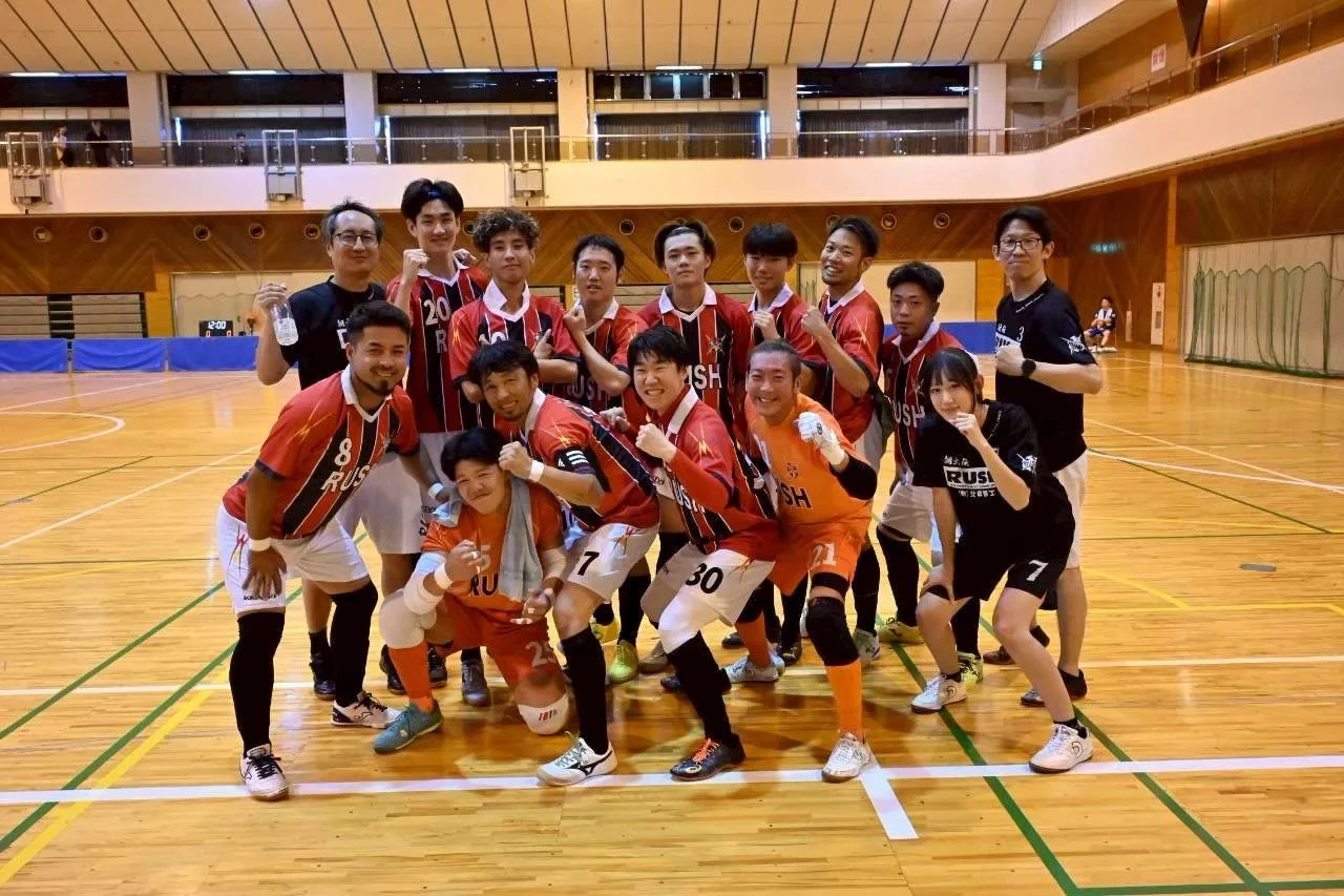 赤と黒の縦じまの昇華ユニフォームを着て、体育館に集合したフットサルチームの選手たち
