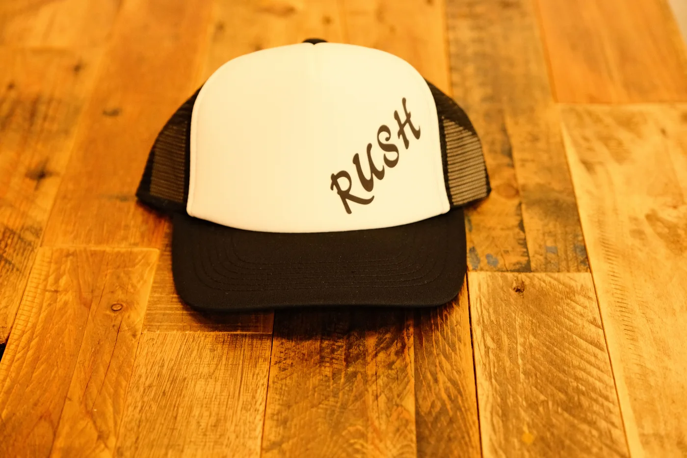 白いフロントにRUSHの筆記体ロゴをプリントした黒のメッシュキャップ
