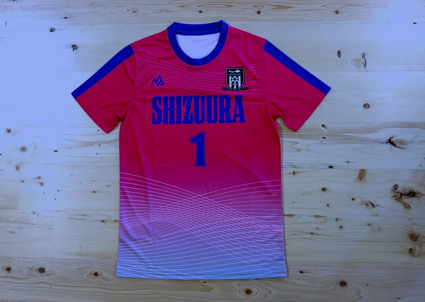ピンクから白へグラデーションするゴールキーパー用のサッカーユニフォームを平置きで撮った写真