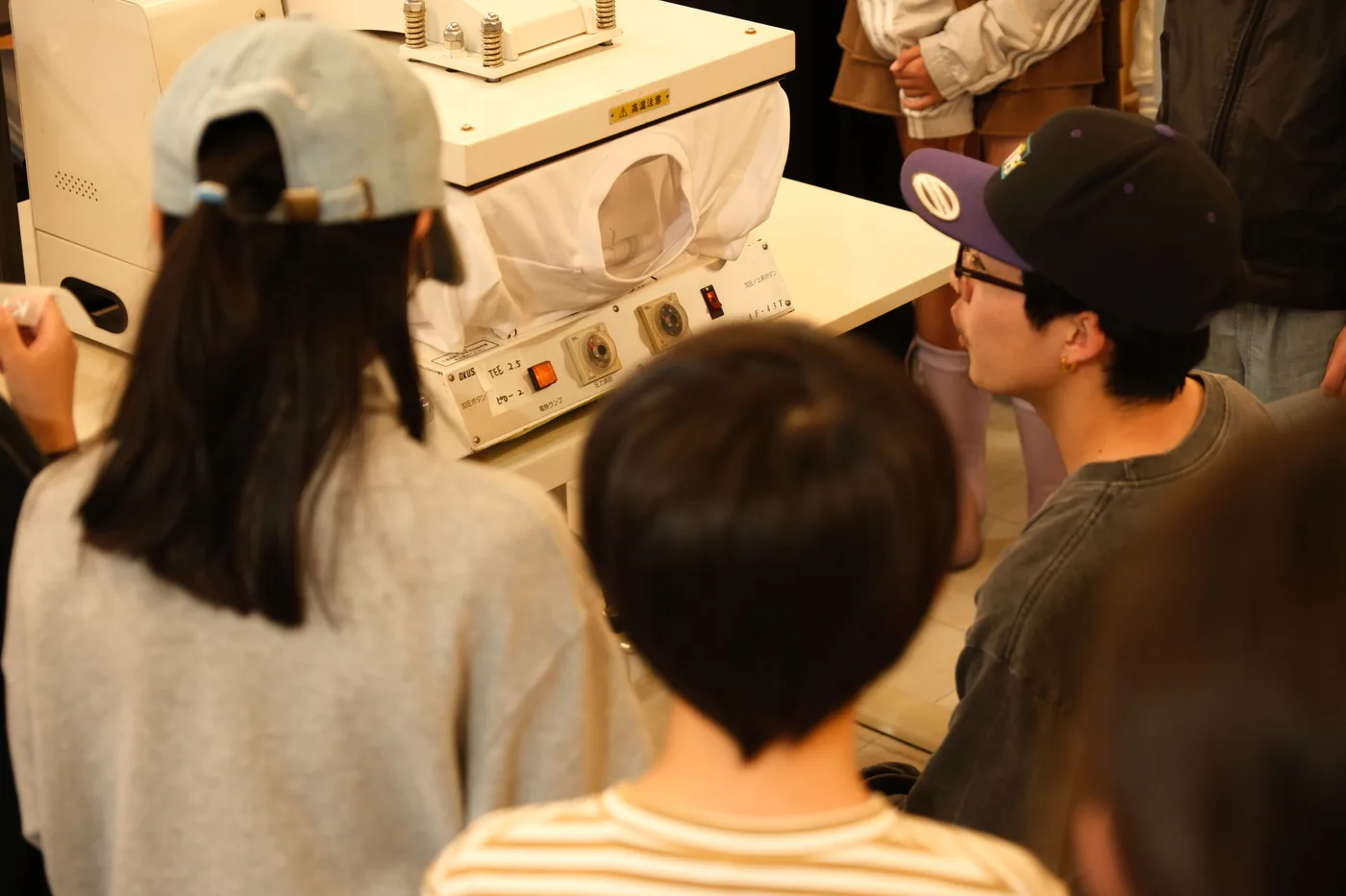 ヒートプレス機のまわりに集まってプリントの様子を見る子どもたち